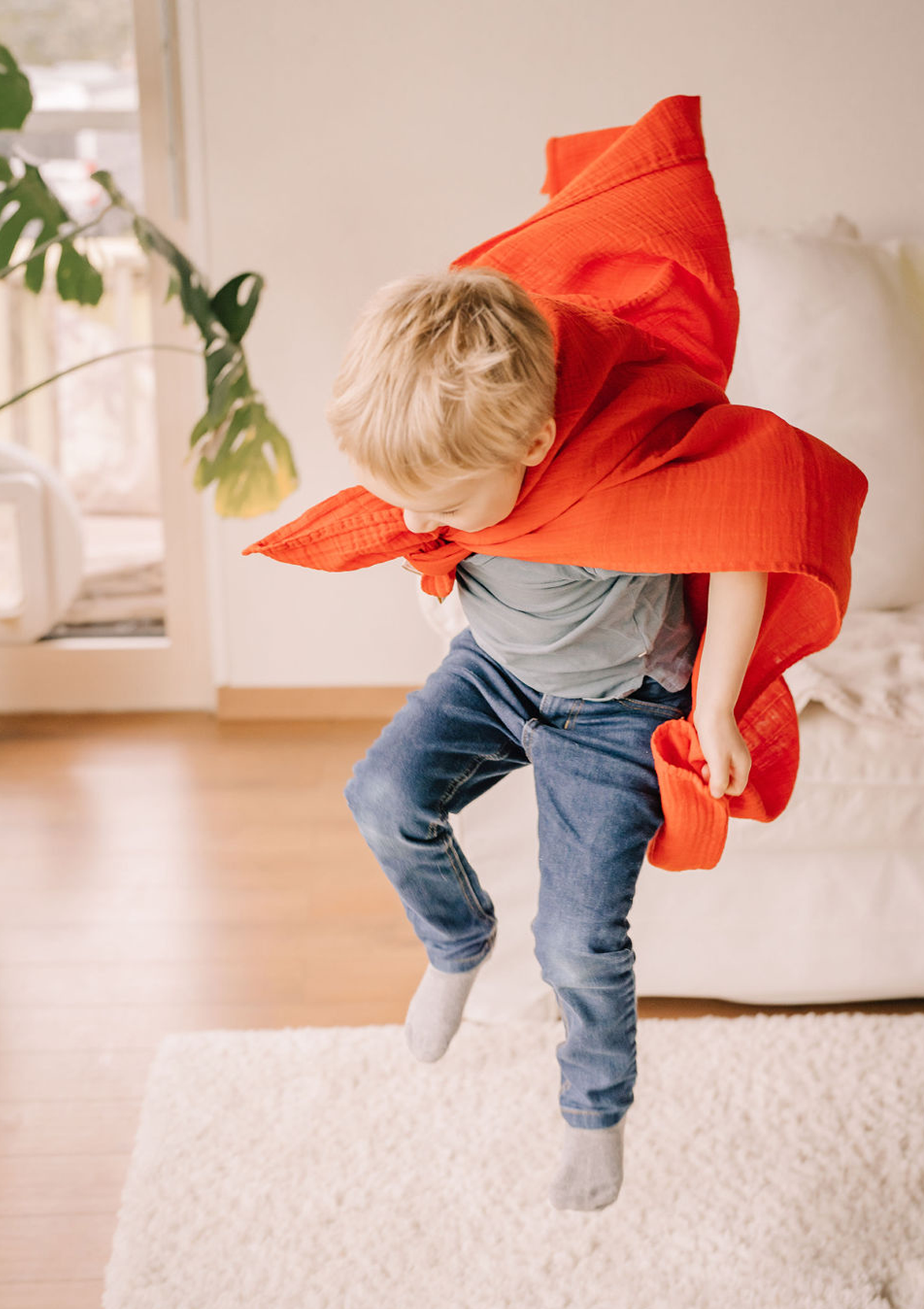 Junge spielt Superman mit rotem Musselin-Tuch