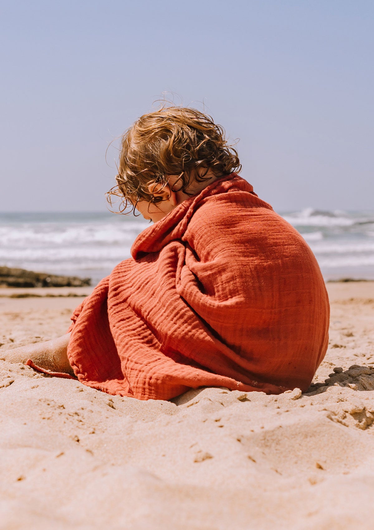 Kleinkind am Strand mit Petit Stellou NOOSHI Tuch rostrot Brick